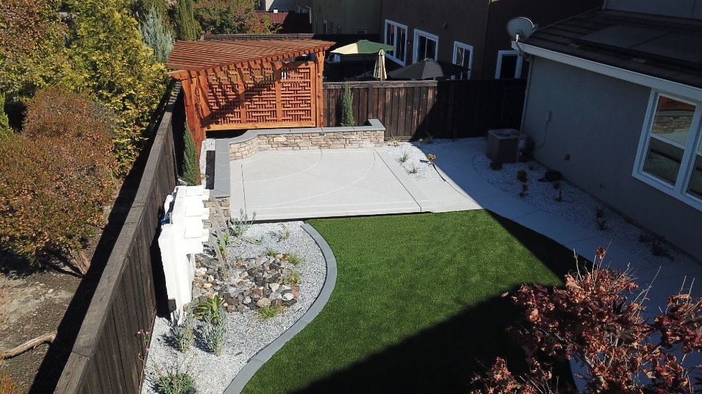 Backyard with wooden pergola, concrete patio, artificial turf and decorative rock landscaping