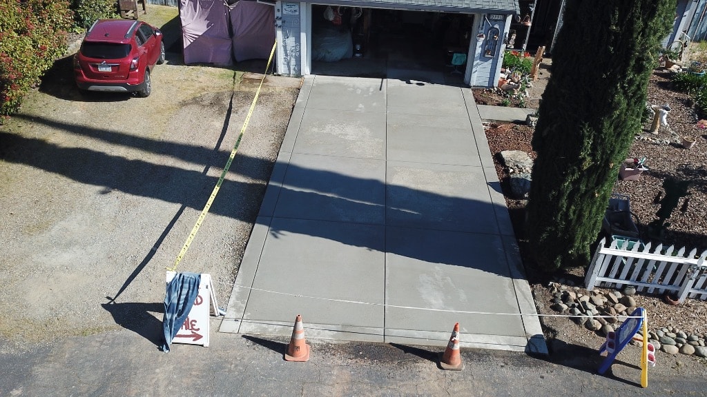 Freshly poured concrete driveway apron with traffic cones, aerial view